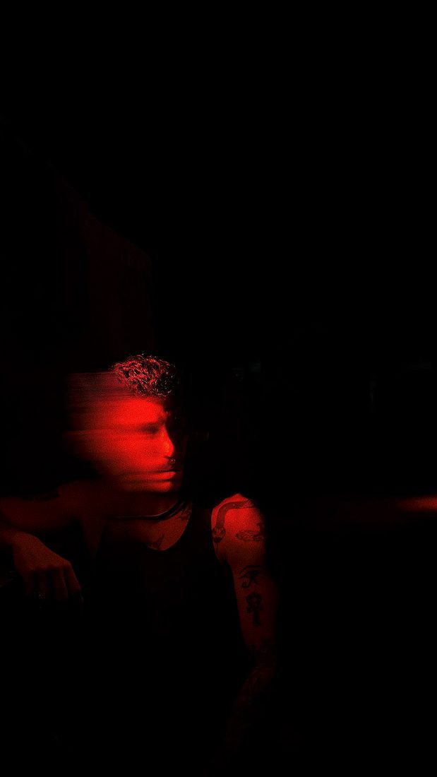 A figure lit in red against black, his face blurred by movement.